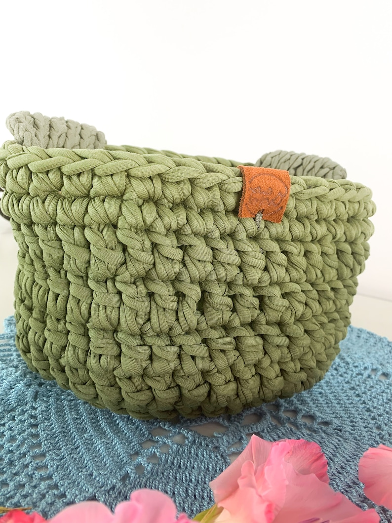 May include: A green crocheted basket with two gray fabric handles and a brown leather tag that says "Handmade with Love".