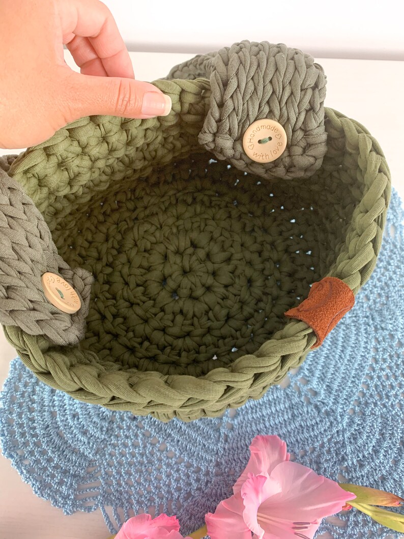 May include: A green crocheted basket with two fabric handles and wooden buttons that say "handmade with love".