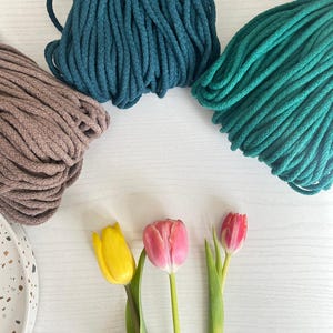 May include: Three spools of cotton rope in teal, dark green, and brown colors. Three tulips in yellow, pink, and red are arranged in a row on a white surface.