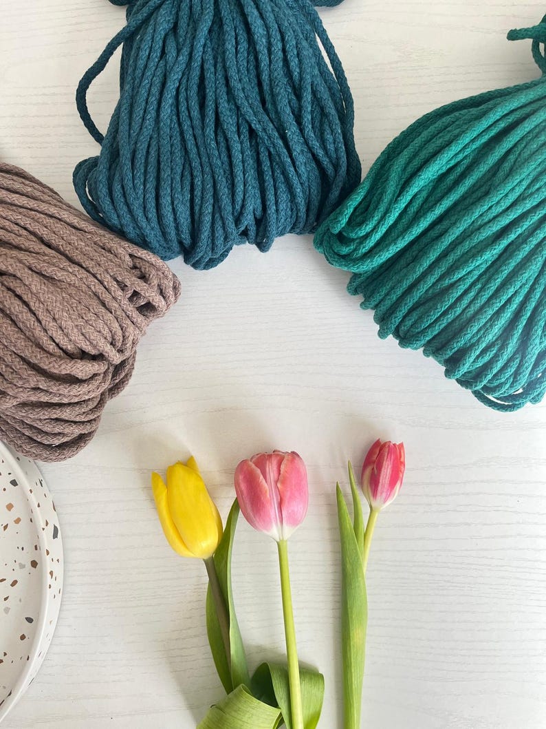 May include: Three spools of cotton rope in teal, dark green, and brown colors. Three tulips in yellow, pink, and red are arranged in a row on a white surface.