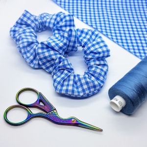 May include: Two blue and white gingham hair scrunchies with a rainbow iridescent pair of scissors and a blue spool of thread labelled "120 100%"