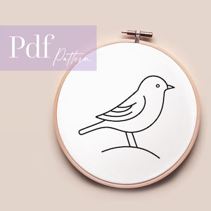 May include: A minimalist embroidery hoop featuring a black line drawing of a bird. The bird is perched on a small hill, with the text "Pdf Pattern" in a lavender box in the upper left corner. The hoop is made of wood.