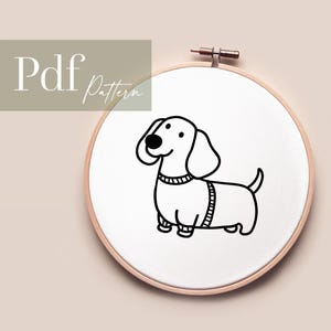 Könnte beinhalten: Schwarz-weiß-Zeichnung eines Dackels mit Pullover auf einem weißen Stickrahmen.