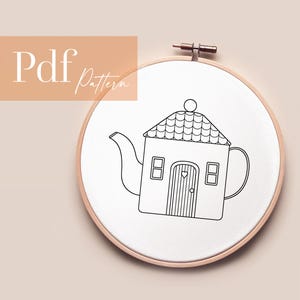 Op de afbeelding: Borduurring met een zwarte omtrek tekening van een theepot-vormig huis. Het ontwerp omvat een schoorsteen, ramen en een hartvormige deur. De woorden "Pdf Pattern" staan in de linkerbovenhoek.