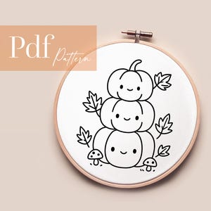 Op de afbeelding: Een zwart-witte borduurring met een stapel pompoenontwerp, bladeren en paddenstoelen. Het ontwerp heeft lachende gezichten. De tekst "Pdf Pattern" staat in de linkerbovenhoek. De ring staat tegen een neutrale achtergrond.