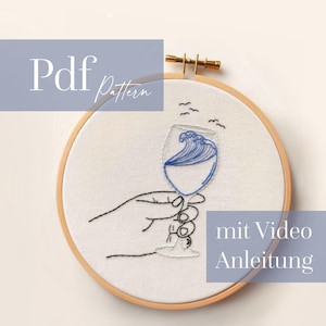 May include: Embroidered hoop art featuring a wine glass with a blue wave design, held by a hand. The text "Pdf Pattern" is in the upper left, and "mit Video Anleitung" is in the lower right. The embroidery is set in a wooden hoop.