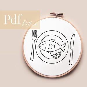 Könnte beinhalten: Stickrahmen mit weißem Stoff mit einer schwarzen Strichzeichnung eines Fisches auf einem Teller mit Gabel und Messer. Eine Zitronenscheibe befindet sich neben dem Fisch. Der Text "Pdf Pattern" befindet sich oben links.