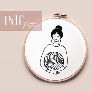 Könnte beinhalten: Eine Schwarz-Weiß-Strichzeichnung einer Person, die einen Wollknäuel hält, in einem hölzernen Stickrahmen. Der Text "Pdf Pattern" befindet sich in der oberen linken Ecke. Die Person hat die Augen geschlossen und lächelt.