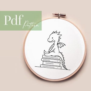 Könnte beinhalten: Schwarz-weiß-Zeichnung eines Cartoon-Drachen, der auf einem Stapel Bücher sitzt. Der Drache hat einen langen Schwanz und Flügel. Das Bild befindet sich in einem weißen Stickrahmen.