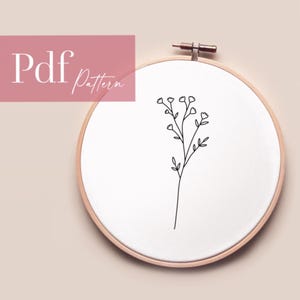 Könnte beinhalten: Eine Schwarzweiß-Zeichnung einer einfachen Blume mit kleinen Blüten auf weißem Hintergrund in einem hölzernen Stickrahmen.