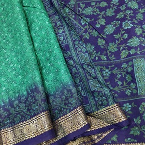 Könnte beinhalten: Ein Textilstoff mit einem leuchtend grünen Bereich mit kleinem weißem Blumenmuster und einem tiefvioletten Bereich mit einem größeren, komplizierten Blumenmuster. Der Stoff ist mit einer breiten, verzierten goldfarbenen Borte am unteren Rand versehen.