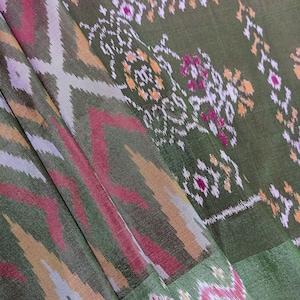Pode incluir: Tecido estampado em verde, vermelho e branco com um design tecido. O tecido tem um brilho sutil e uma textura macia.