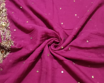 May include: A pink fabric with gold sequins and embroidery. The fabric is folded and draped, showing the texture and detail of the embellishments.