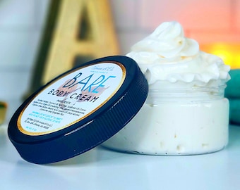 May include: A black jar with a white lid containing a white body cream. The jar has a gold label with the text "BARE BODY CREAM" and a list of ingredients. The cream is whipped and fluffy.