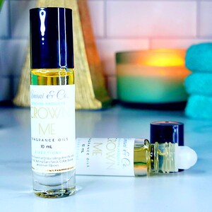 May include: Two clear glass bottles with black roll-on tops containing a yellow liquid. The bottles are labeled "Amani & Co. Skincare Products Crown Me Fragrance Oils 10 mL Directions Essential Oils by rolling directly onto pulse points/Neck, Collar Bones and Inner Elbows."