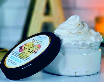 May include: A white body cream in a clear jar with a black lid. The lid has a label that says "Mango Obsession Body Cream".