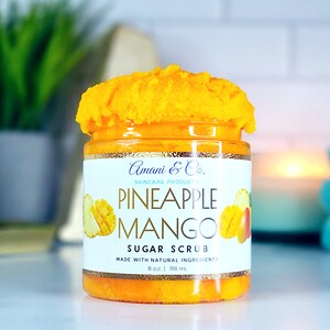 May include: A glass jar of pineapple mango sugar scrub with a white label that reads "Amani & Co. Skincare Products Pineapple Mango Sugar Scrub Made with Natural Ingredients 8 oz. 118 ml".