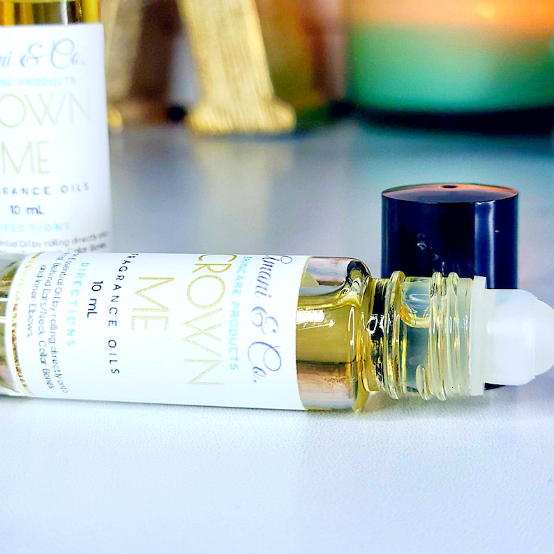 May include: A clear glass roll-on bottle with a black cap and a white label. The label says "Imani & Co. Skincare Products Crown Me Fragrance Oils 10 mL Directions".