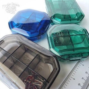 May include: Three clear plastic containers with multiple compartments. The containers are blue, green, and gray. The containers are used for organizing small items, such as beads, buttons, or sewing supplies.