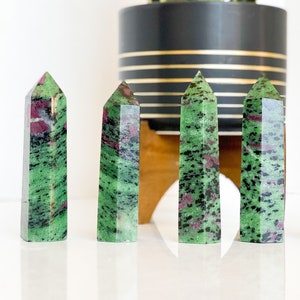 May include: Five green and pink zultanite crystal points, also known as zultanite gemstone, arranged in a row on a white surface.