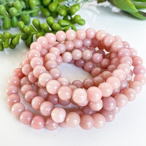 May include: A stack of pink opal bead bracelets. The beads are round and smooth, and the bracelets are made with elastic.