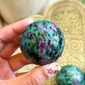 Könnte beinhalten: Nahaufnahme einer grünen und rosafarbenen Edelsteinkugel. Die Kugel ist glatt und poliert und hat ein gesprenkeltes Muster aus Grün, Schwarz und Rosa.