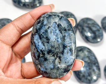 May include: An oval-shaped polished labradorite stone featuring a dark gray base with iridescent blue flashes and black inclusions. The surface is smooth and reflective, showcasing natural mineral patterns throughout the stone's crystalline structure.