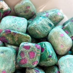 May include: A collection of tumbled green and pink ruby zoisite stones. The stones are smooth and polished, with a variety of shapes and sizes.