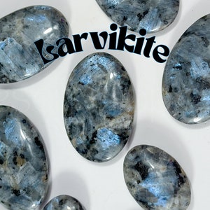 May include: A collection of six smooth, oval-shaped labradorite stones. The stones are a mix of grey and blue with iridescent flashes of colour. The stones are arranged on a white surface. The word "Labradorite" is written in blue letters across the image.