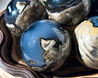 May include: A collection of six polished agate spheres in a wooden bowl. The spheres are various shades of blue, gray, and brown with intricate patterns.