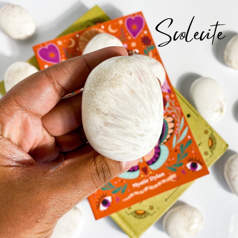 May include: A white, smooth, round, polished scolecite stone with a striated pattern.