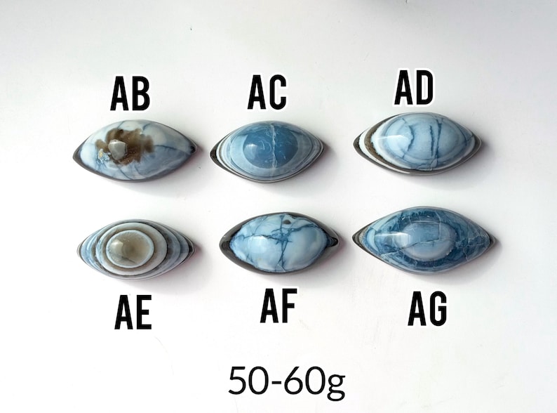 May include: Six oval-shaped blue and white stones labelled AB, AC, AD, AE, AF, and AG. Each stone features unique patterns and colour variations. The text 50-60g is displayed at the bottom, indicating the weight range for these polished stones.