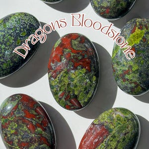 May include: Five smooth, oval-shaped stones with a green, black, and red mottled pattern. The stones are labeled "Dragons Bloodstone".
