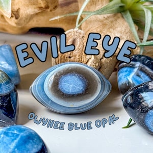 May include: Polished Owyhee blue opal stones with natural banding, featuring a central eye-like pattern. The text EVIL EYE and OWYHEE BLUE OPAL is overlaid in light blue letters. The stones display shades of deep blue, gray, and white.