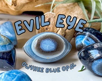 Puede incluir: Piedras de ópalo azul de Owyhee pulidas con bandas naturales, con un patrón central en forma de ojo. El texto EVIL EYE y OWYHEE BLUE OPAL está superpuesto en letras azul claro. Las piedras muestran tonos de azul oscuro, gris y blanco.