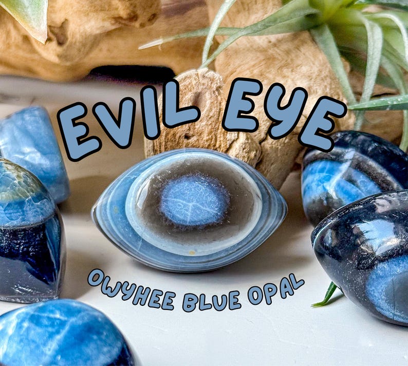 May include: Polished Owyhee blue opal stones with natural banding, featuring a central eye-like pattern. The text EVIL EYE and OWYHEE BLUE OPAL is overlaid in light blue letters. The stones display shades of deep blue, grey, and white.