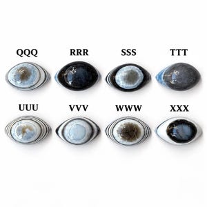 May include: Eight oval-shaped cabochons arranged in two rows, each featuring distinct concentric patterns or solid dark tones. The pieces are labelled QQQ, RRR, SSS, TTT, UUU, VVV, WWW, and XXX. These smooth, polished stones display varied shades of blue, grey, black, and white.