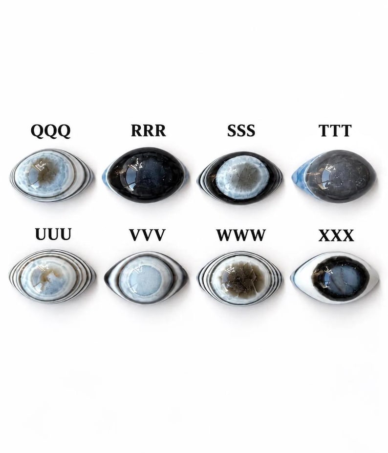 May include: Eight oval-shaped cabochons arranged in two rows, each featuring distinct concentric patterns or solid dark tones. The pieces are labelled QQQ, RRR, SSS, TTT, UUU, VVV, WWW, and XXX. These smooth, polished stones display varied shades of blue, grey, black, and white.