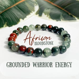 Könnte beinhalten: Ein Armband aus afrikanischem Blutstein. Das Armband besteht aus roten, grünen und schwarzen Perlen. Der Text "African Bloodstone" und "Grounded Warrior Energy" ist auf dem Bild zu sehen.