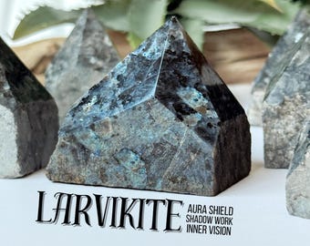 May include: A collection of Larvikite crystal pyramids with a dark gray and blue iridescence. The crystals are faceted and have a rough, natural texture. Text on the image reads "LARVIKITE" and "AURA SHIELD, SHADOW WORK, INNER VISION."