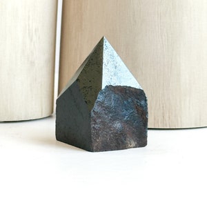 May include: A dark gray, pyramid-shaped crystal with a rough, textured surface.