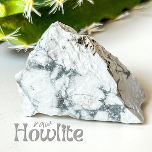 May include: A raw Howlite stone, white with grey veining, on a white surface. The stone is rough and has an irregular shape.