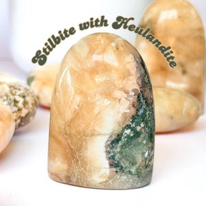 Op de afbeelding: Een glad, licht oranje en groen kristal met de tekst "Stilbite with Heulandite" erboven.