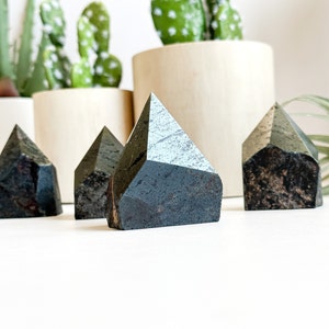 May include: Four black and grey crystal points in the shape of pyramids. The crystals are arranged in a row on a white surface.