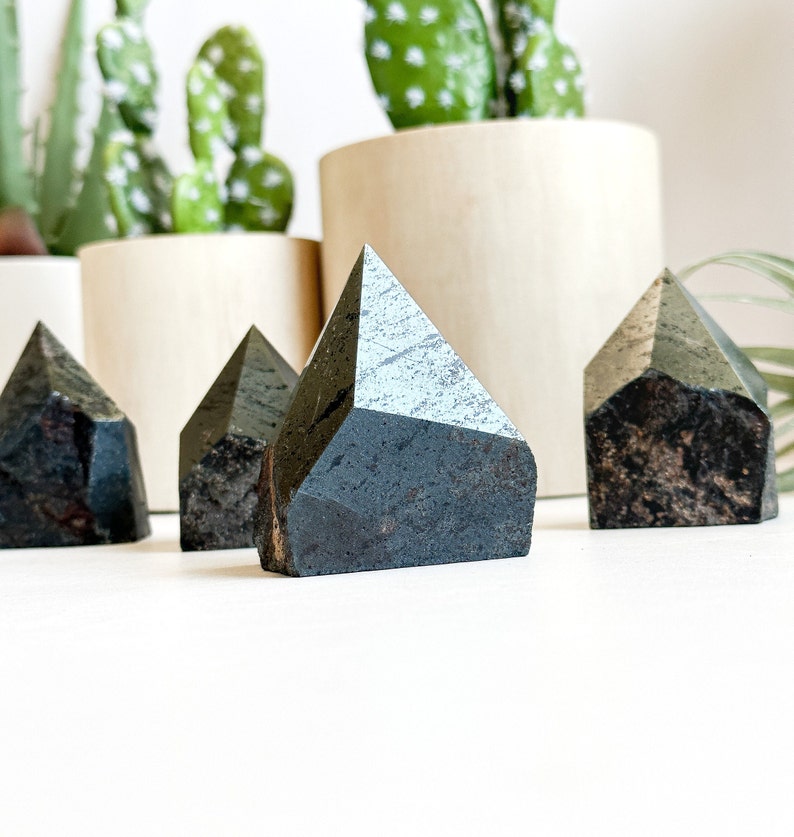 May include: Four black and grey crystal points in the shape of pyramids. The crystals are arranged in a row on a white surface.
