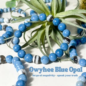 May include: A blue and white Owyhee Blue Opal bracelet with the text "Owyhee Blue Opal let go of negativity. speak your truth".