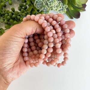 May include: A close-up of a stack of pink opal bead bracelets. The beads are round and smooth, and they have a subtle shimmer.