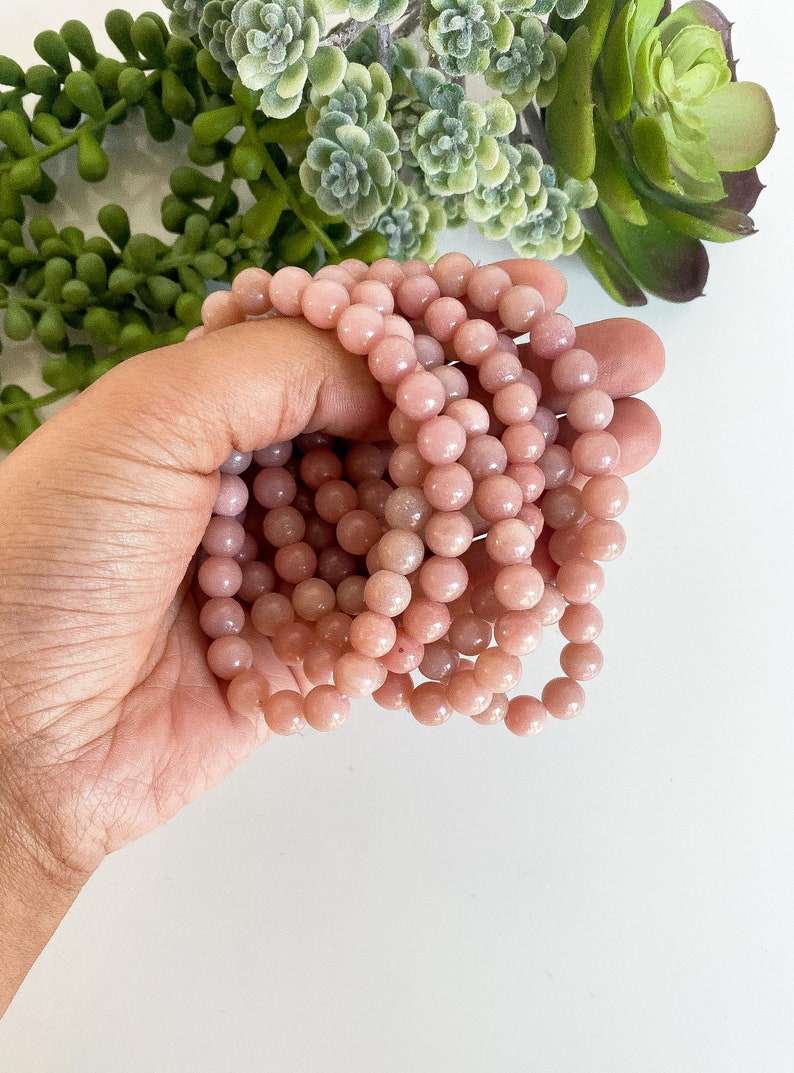 May include: A close-up of a stack of pink opal bead bracelets. The beads are round and smooth, and they have a subtle shimmer.