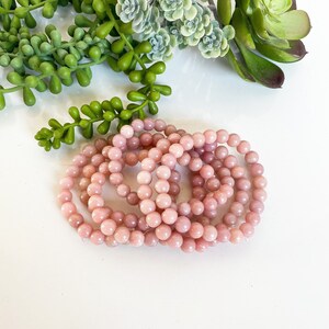 May include: A set of pink opal beaded bracelets. The bracelets are made of small, round beads and are stacked on top of each other.