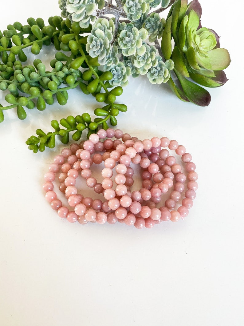 May include: A set of pink opal beaded bracelets. The bracelets are made of small, round beads and are stacked on top of each other.
